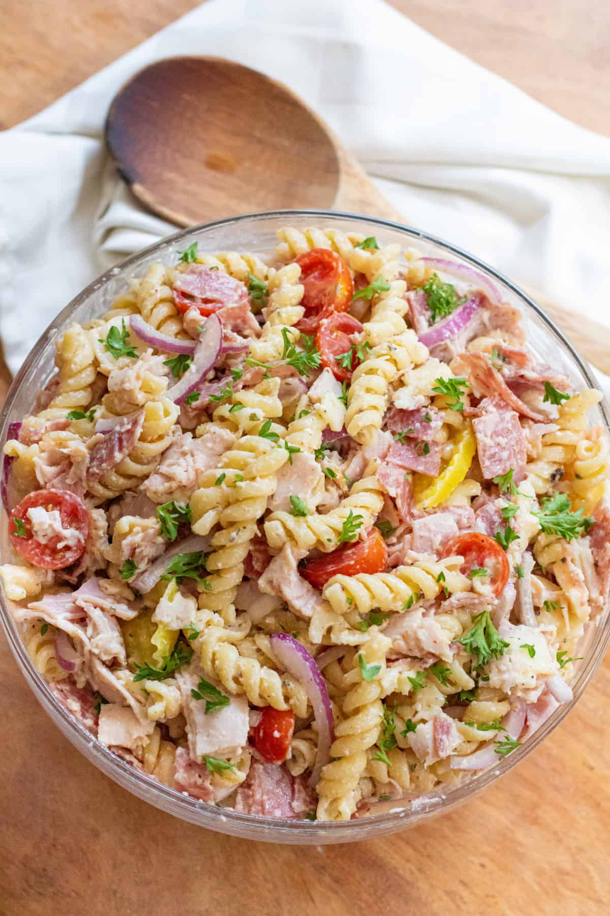 an overhead of a pasta salad with meats, cheese, tomatoes, parsley, and banana peppers.