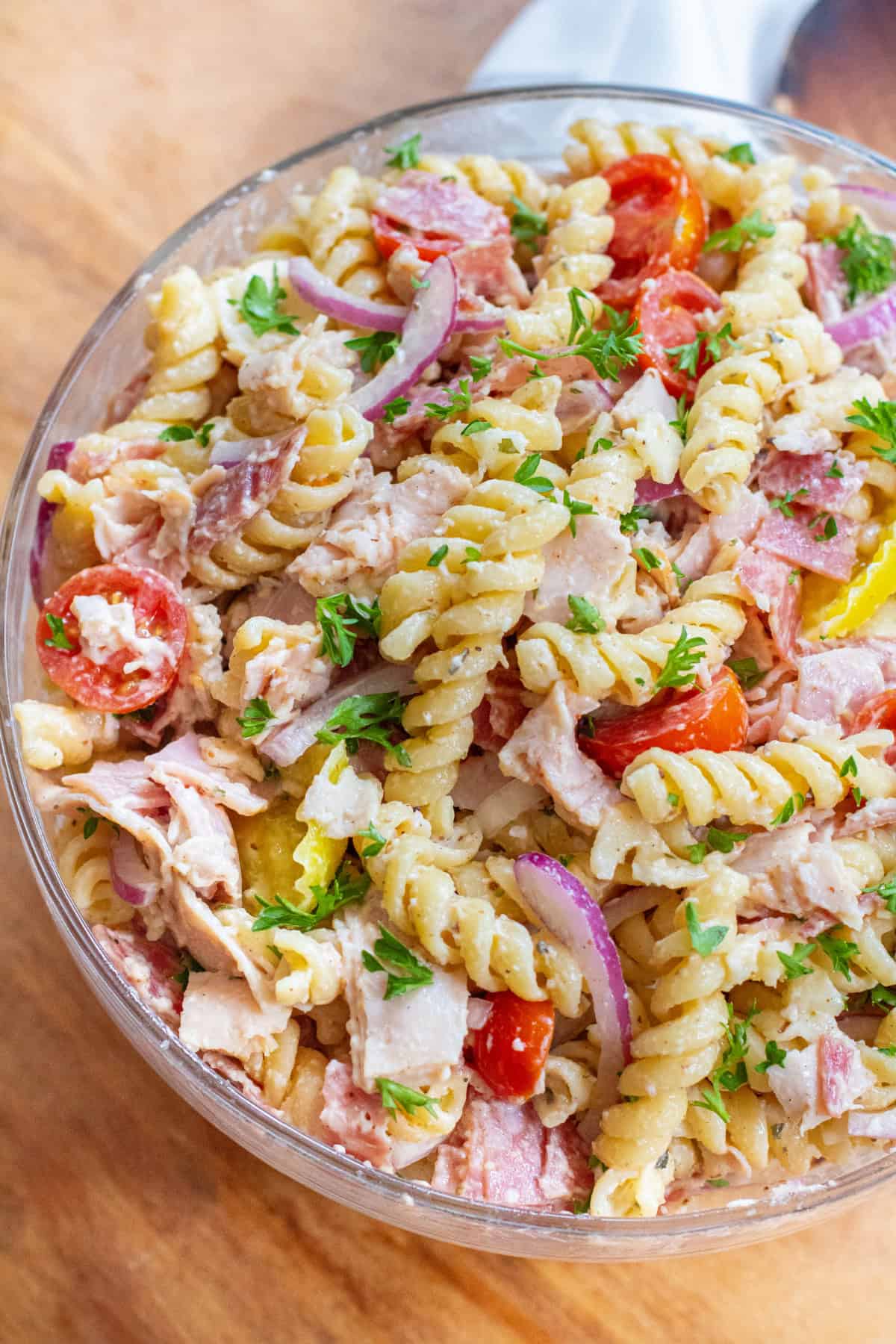 an overhead of a pasta salad with meats, cheese, tomatoes, parsley, and banana peppers.
