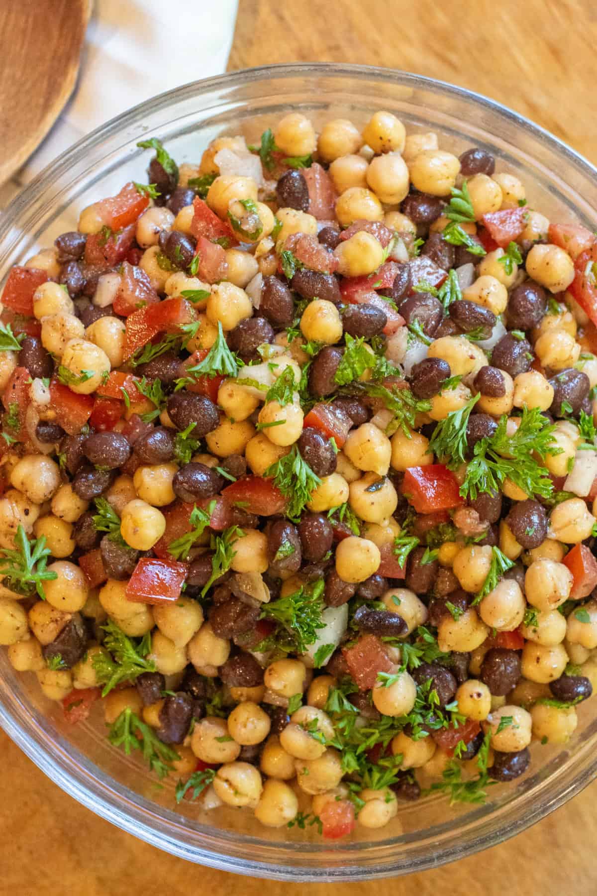 a salad with chickpeas black beans, tomatoes, and parsley.