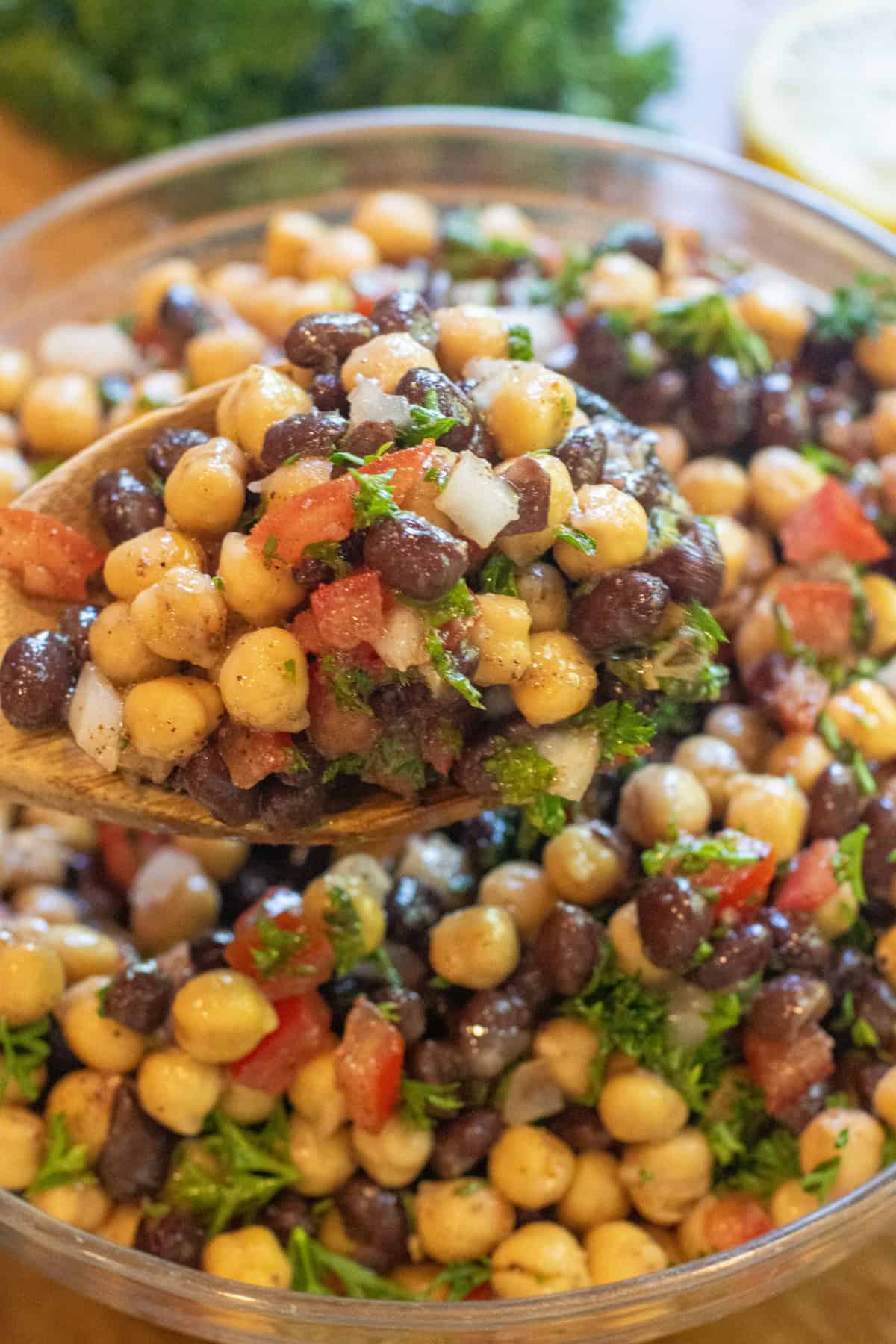 a salad with chickpeas black beans, tomatoes, and parsley with a wooden spoon.