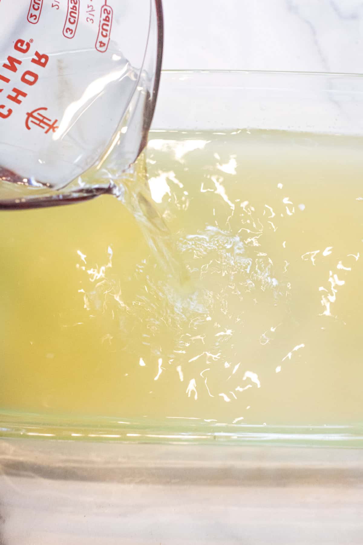 water being poured into a glass baking dish with lemon and basil juice.
