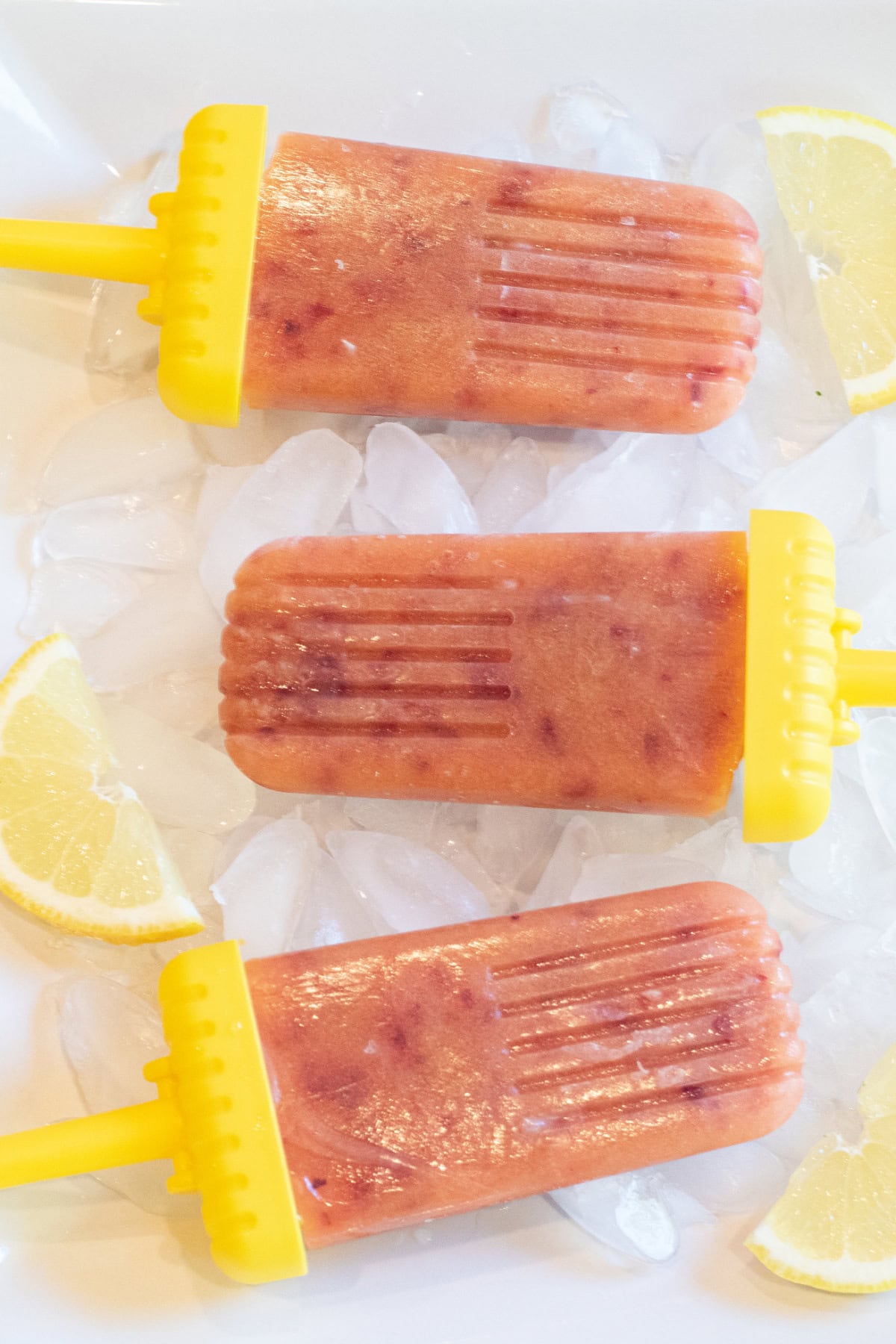 a plate of 3 peach popsicles with lemon slices.