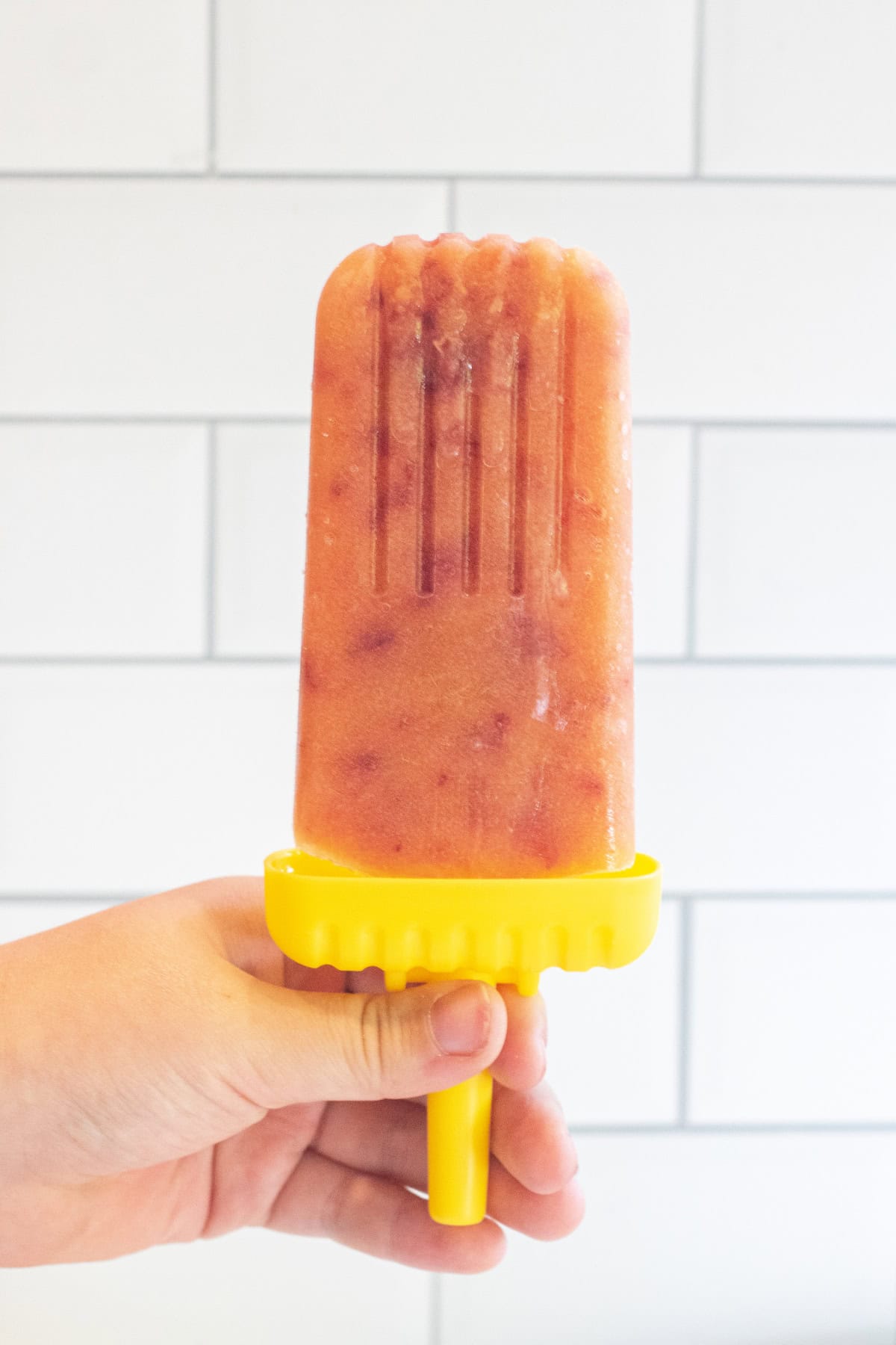 a hand holding a peach lemonade popsicle. 