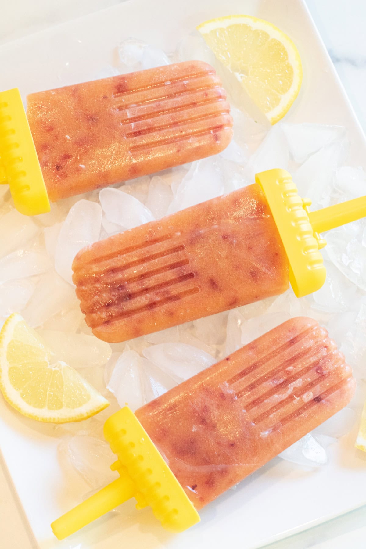 a plate of peach colored popsicles on ice with lemon slices.