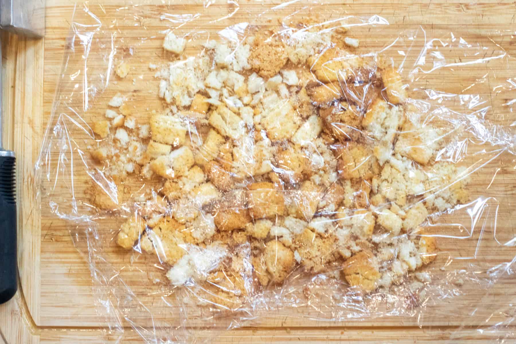 croutons on a cutting board with plastic over it and them broke up a bit under the plastic.