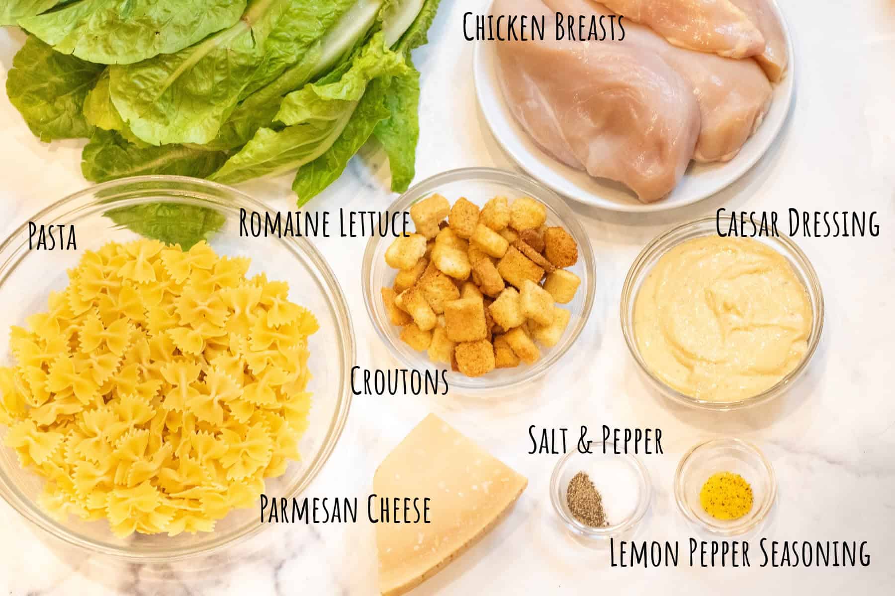 a bowl of farfalle pasta, lettuce, raw chicken, croutons, caesar salad dressing, parmesan cheese, salt and pepper, and lemon pepper seasoning all labeled.