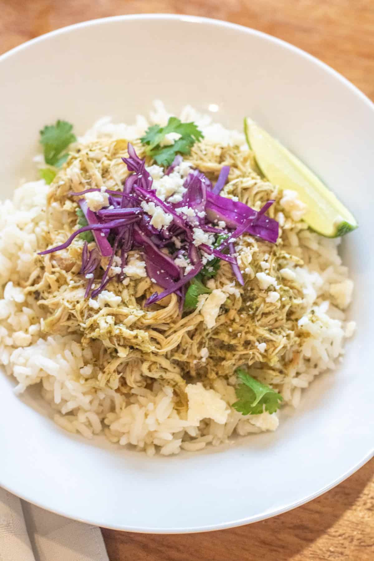 a bowl of rice with shredded chicken on top and purple cabbage, cotija, cilantro, and a lime wedge.