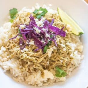a bowl of rice with shredded chicken on top and purple cabbage, cotija, cilantro, and a lime wedge.