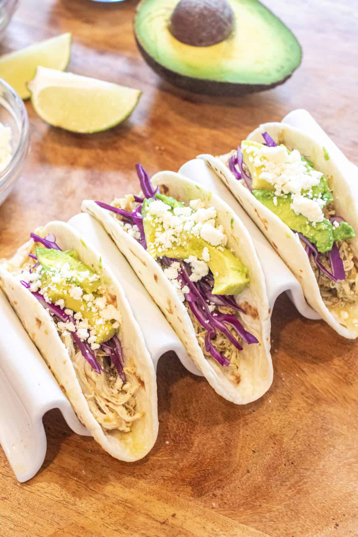 three tacos with shredded chicken, cabbage, avocado, and cotija.