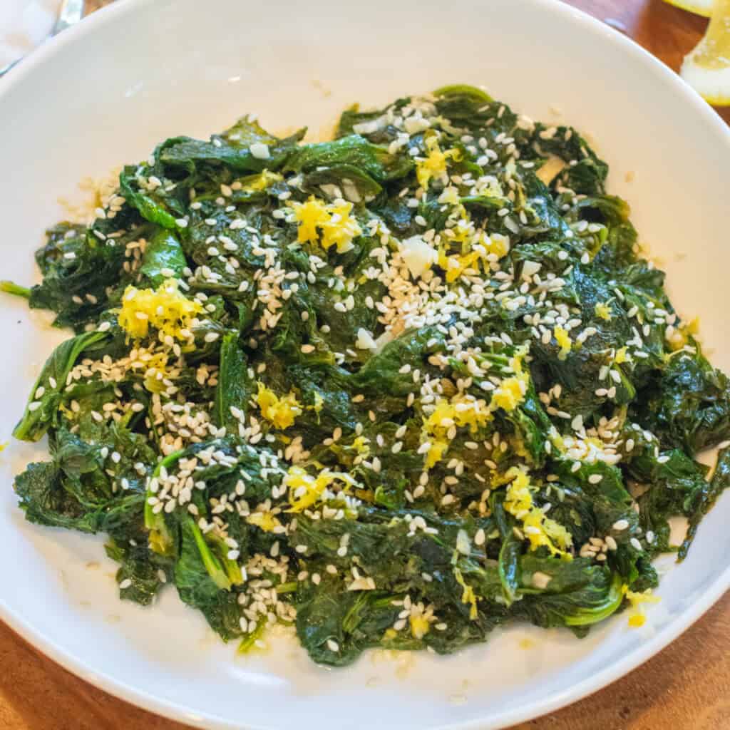 a bowl of cooked mustard greens with sesame seeds and lemon zest.