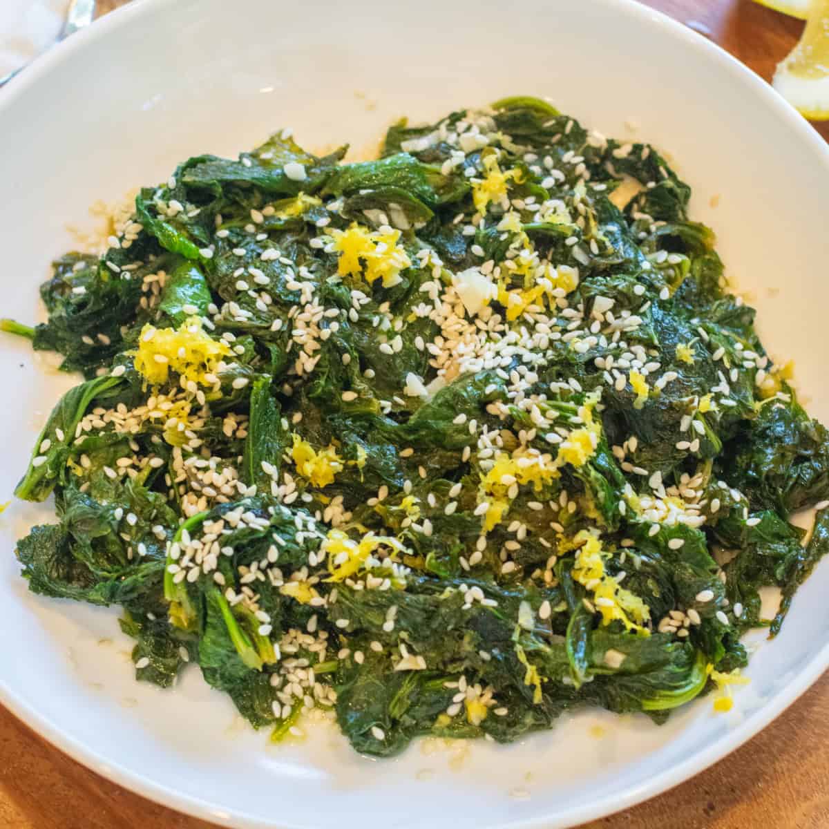 a bowl of cooked mustard greens with sesame seeds and lemon zest.