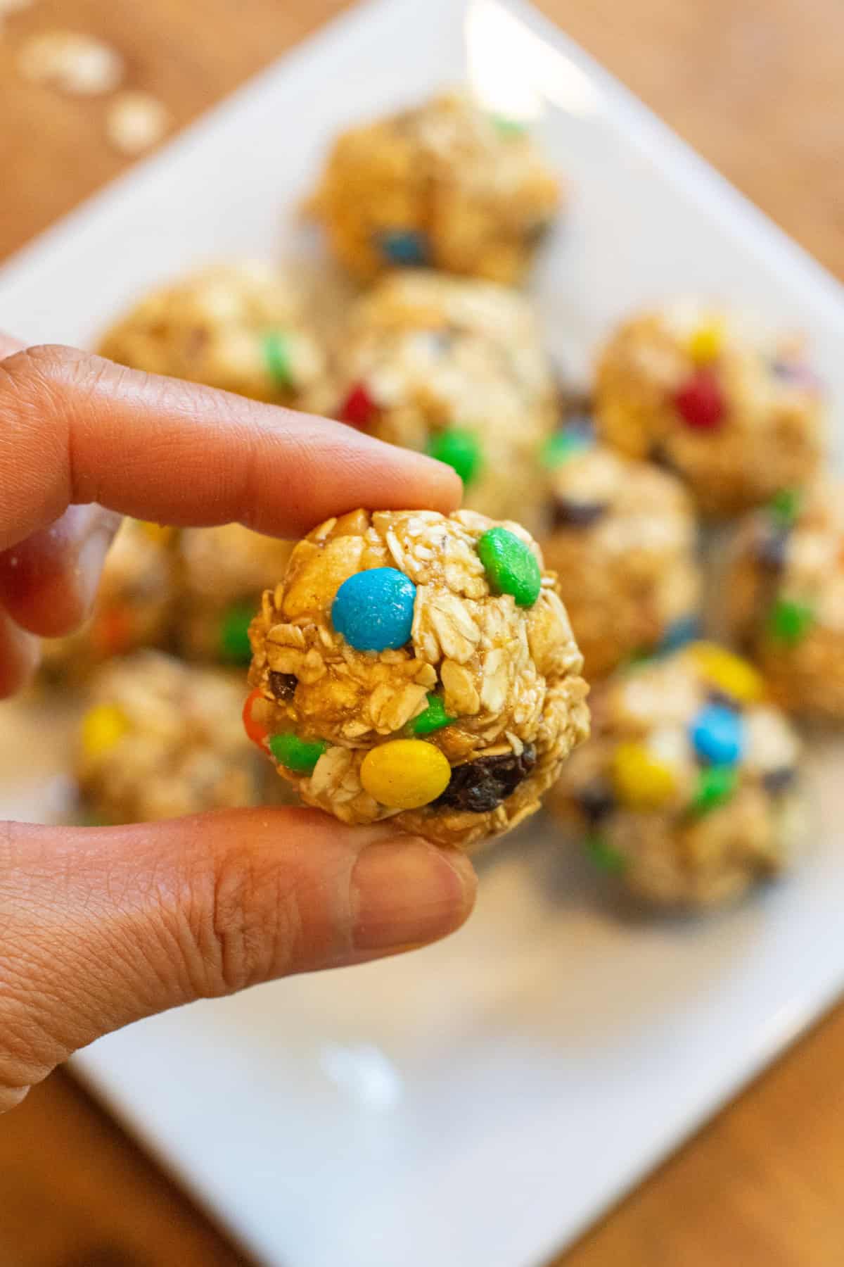 a hand holding an oat ball with m&ms, raisins, and nuts.