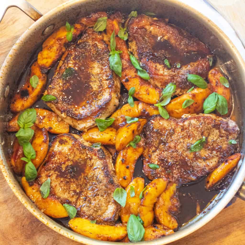 an overhead of a pan of pork chops in butter sauce with peaches and basil.