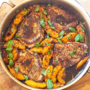 an overhead of a pan of pork chops in butter sauce with peaches and basil.