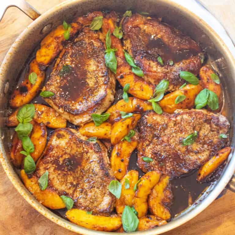 an overhead of a pan of pork chops in butter sauce with peaches and basil.