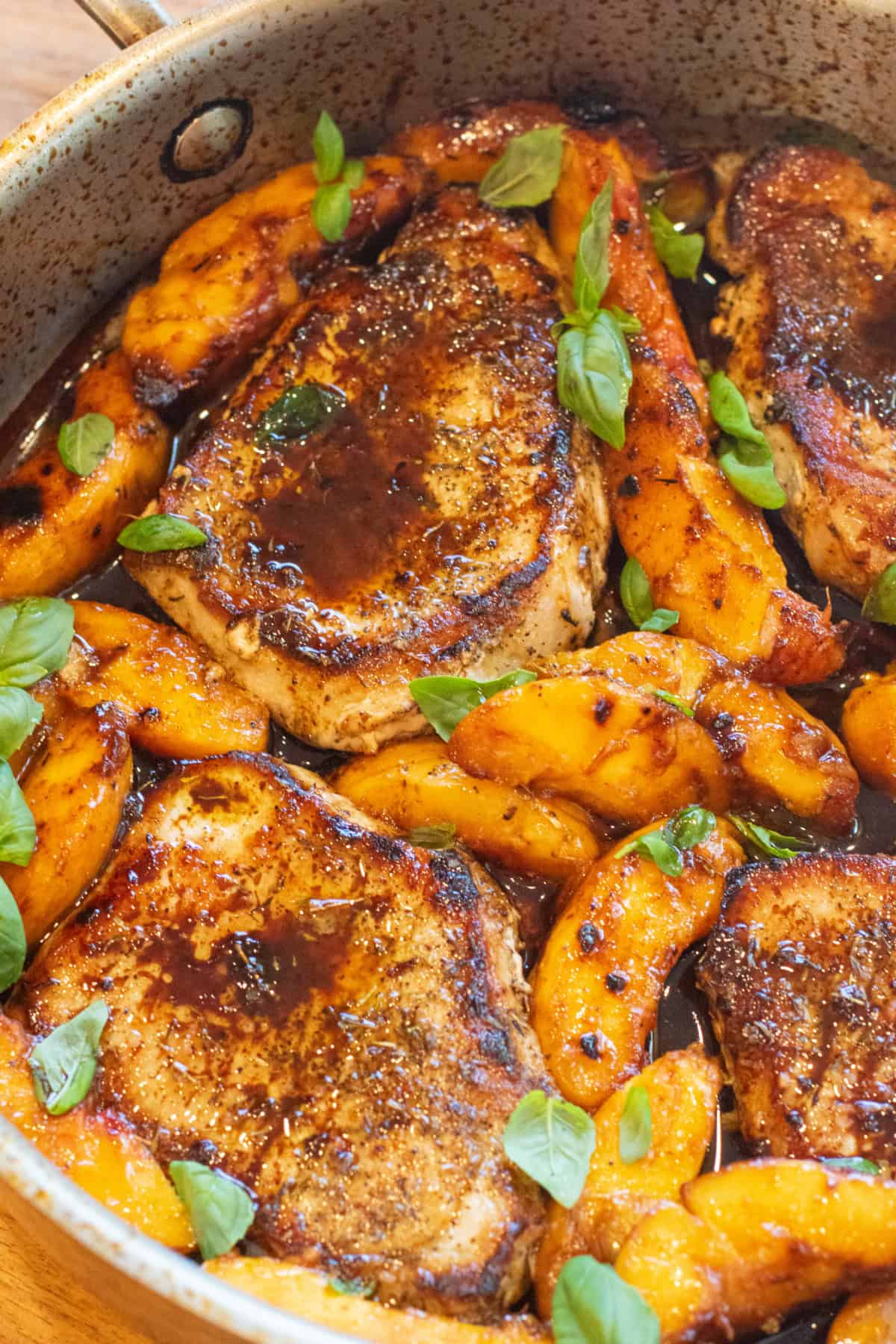 an overhead of a pan of pork chops in butter sauce with peaches and basil.