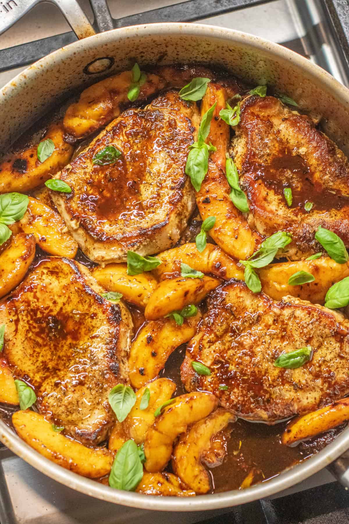 an overhead of a pan of pork chops in butter sauce with peaches and basil.