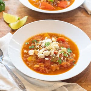 a bowl of lentil pepper stew topped with cotija cheese and cilantro.