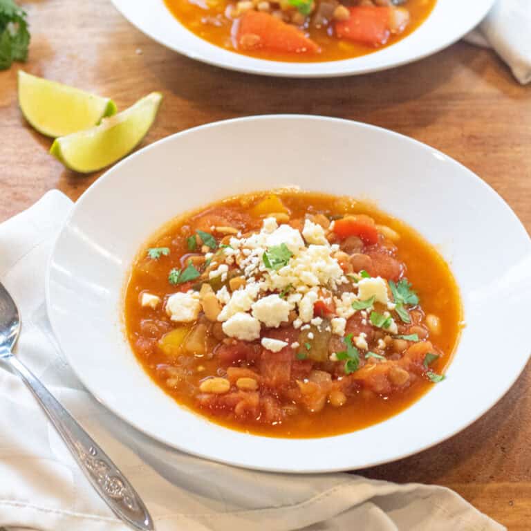 a bowl of lentil pepper stew topped with cotija cheese and cilantro.