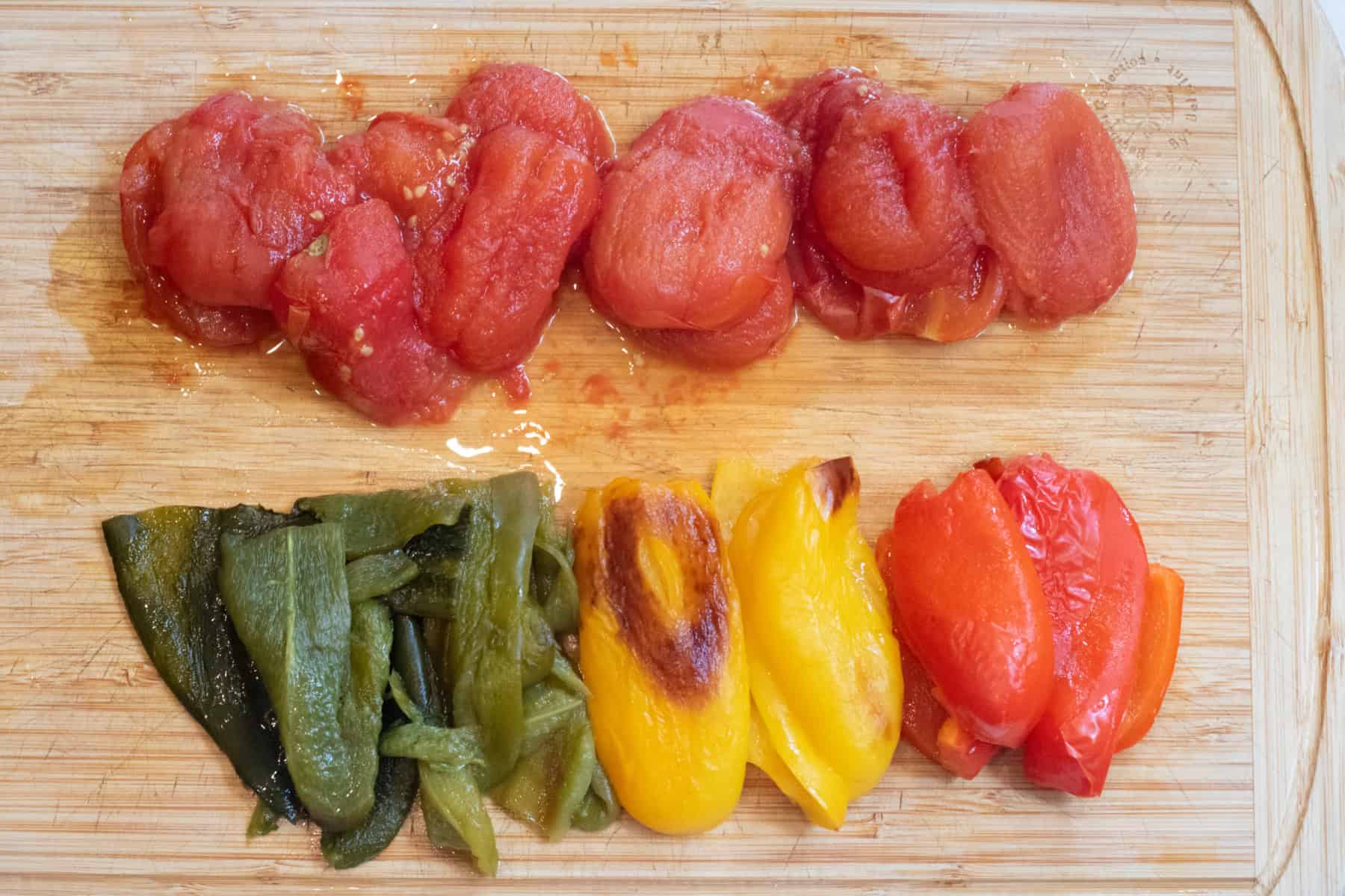 roasted tomatoes and multi colored skinned peppers on a cutting board.