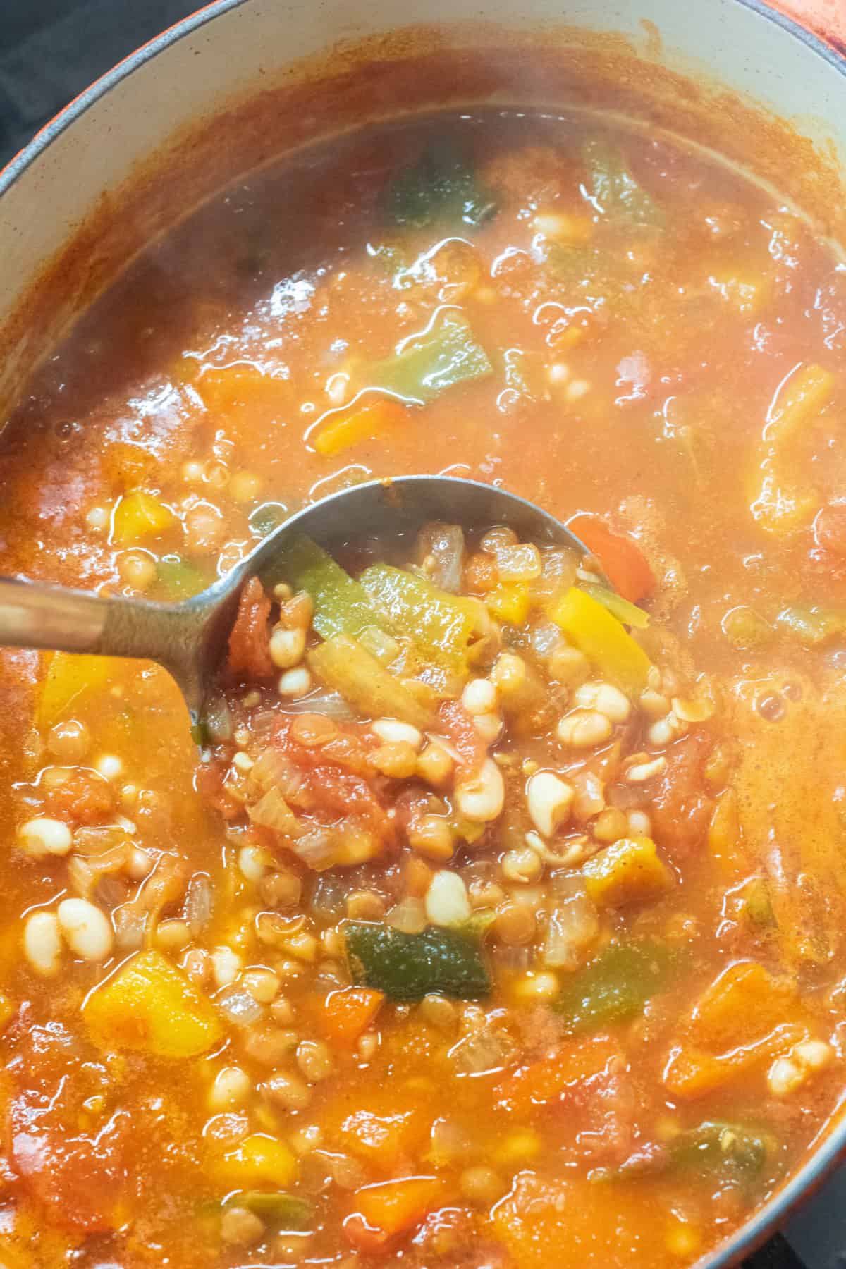 A ladle full of lentil bean and pepper soup in a dutch oven.