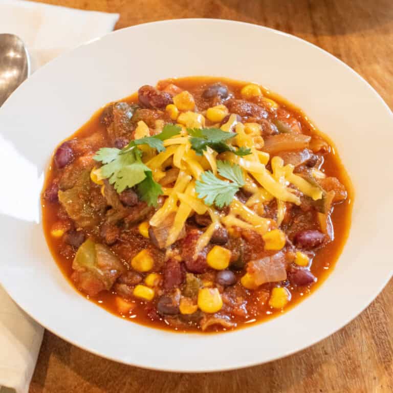 a bowl of vegetarian chili with shredded cheese and cilantro on top.