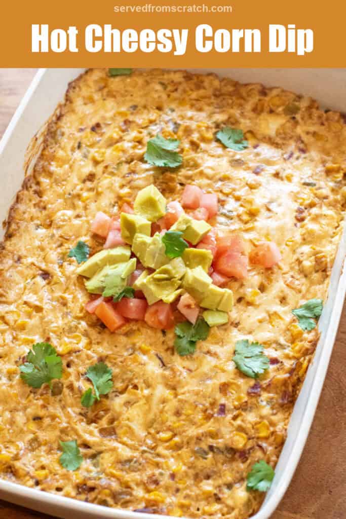 a baking dish of cheesy corn dip topped with diced tomatoes, avocado, and fresh cilantro with Pinterest pin text.