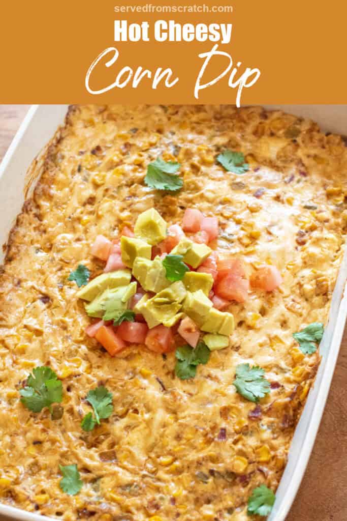a baking dish of cheesy corn dip topped with diced tomatoes, avocado, and fresh cilantro with Pinterest pin text.
