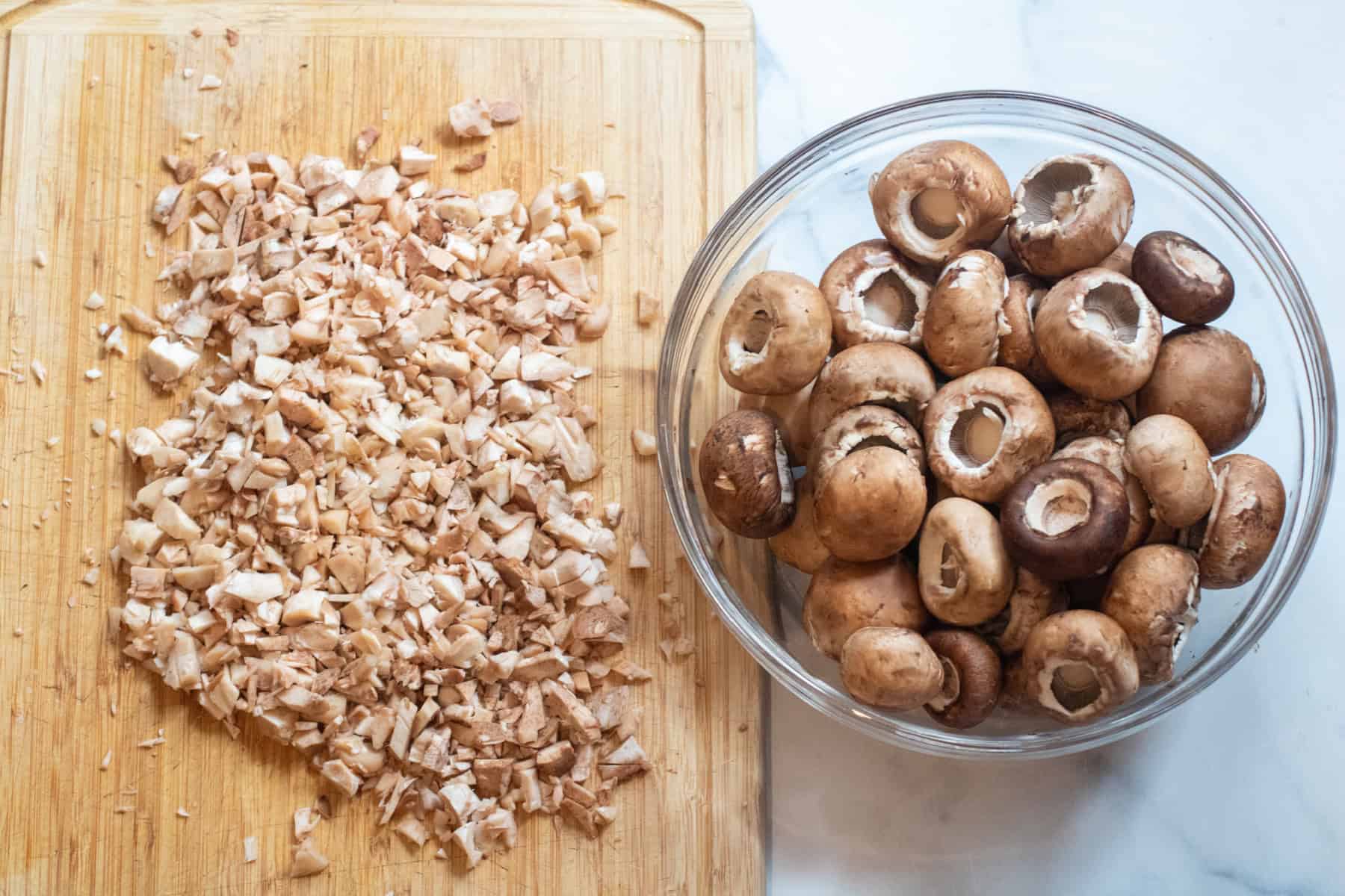 a bowl of mushroom with stems removed and a cutting board of stems all finely chopped.