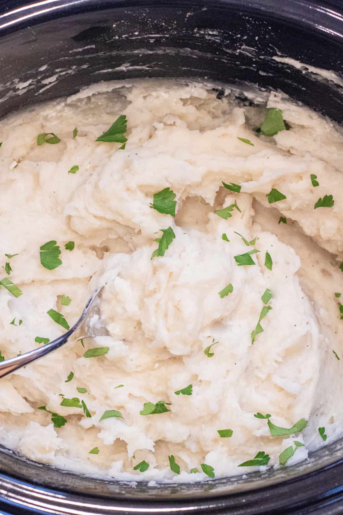a crock pot of creamy mashed potatoes with chopped parsley.