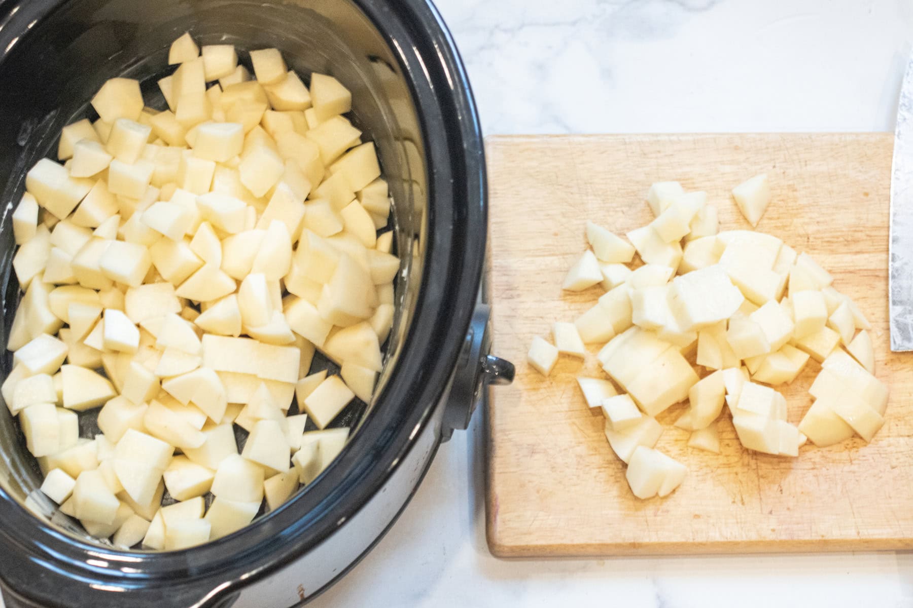 a crock pot of diced potatoes and a cutting board with chopped potatoes.
