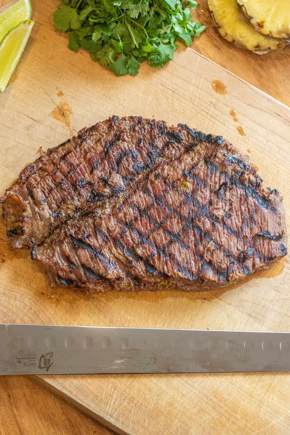 an overhead of a grilled steak on a cutting board next to a knife.