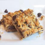 two dessert bars with chocolate chips and coconut layered on a white plate.
