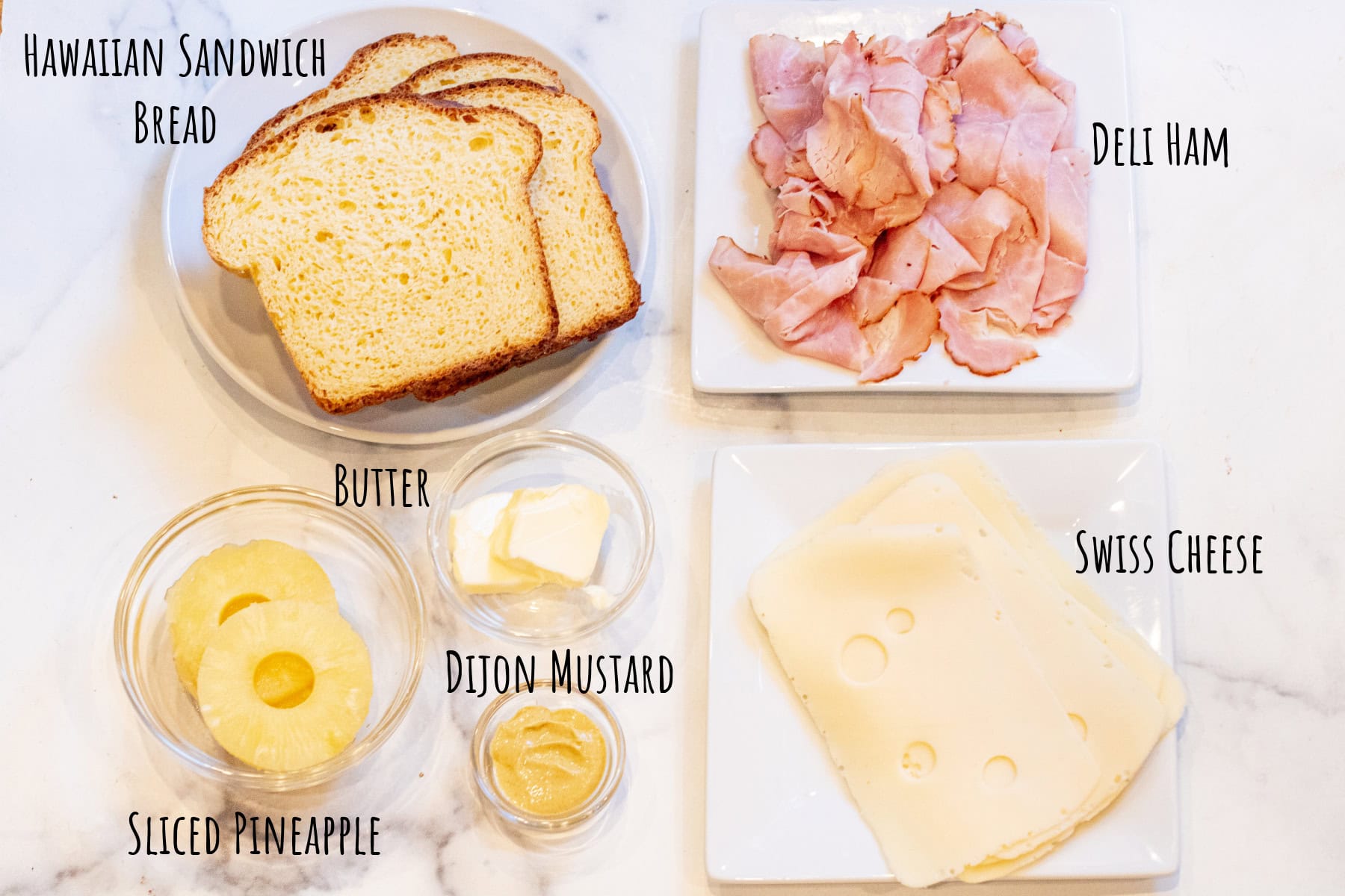 a plate of sliced bread, deli ham, swiss cheese, sliced pineapple, butter, and dijon mustard.