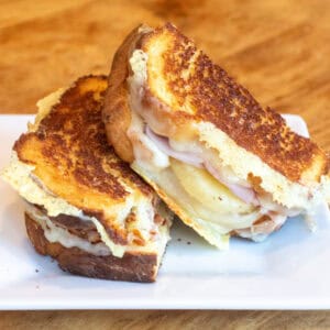 a halved grilled cheese with ham and pineapple stacked on a plate.