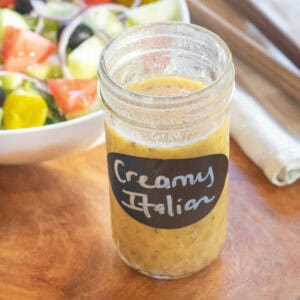 a jar of open italian salad dressing labeled creamy italian in front of a bowl of salad.