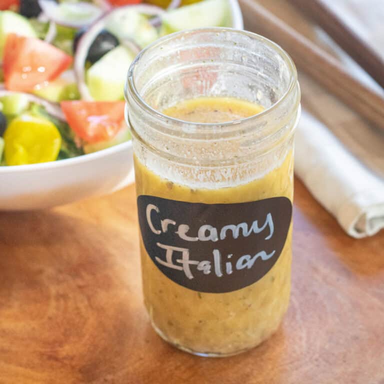 a jar of open italian salad dressing labeled creamy italian in front of a bowl of salad.