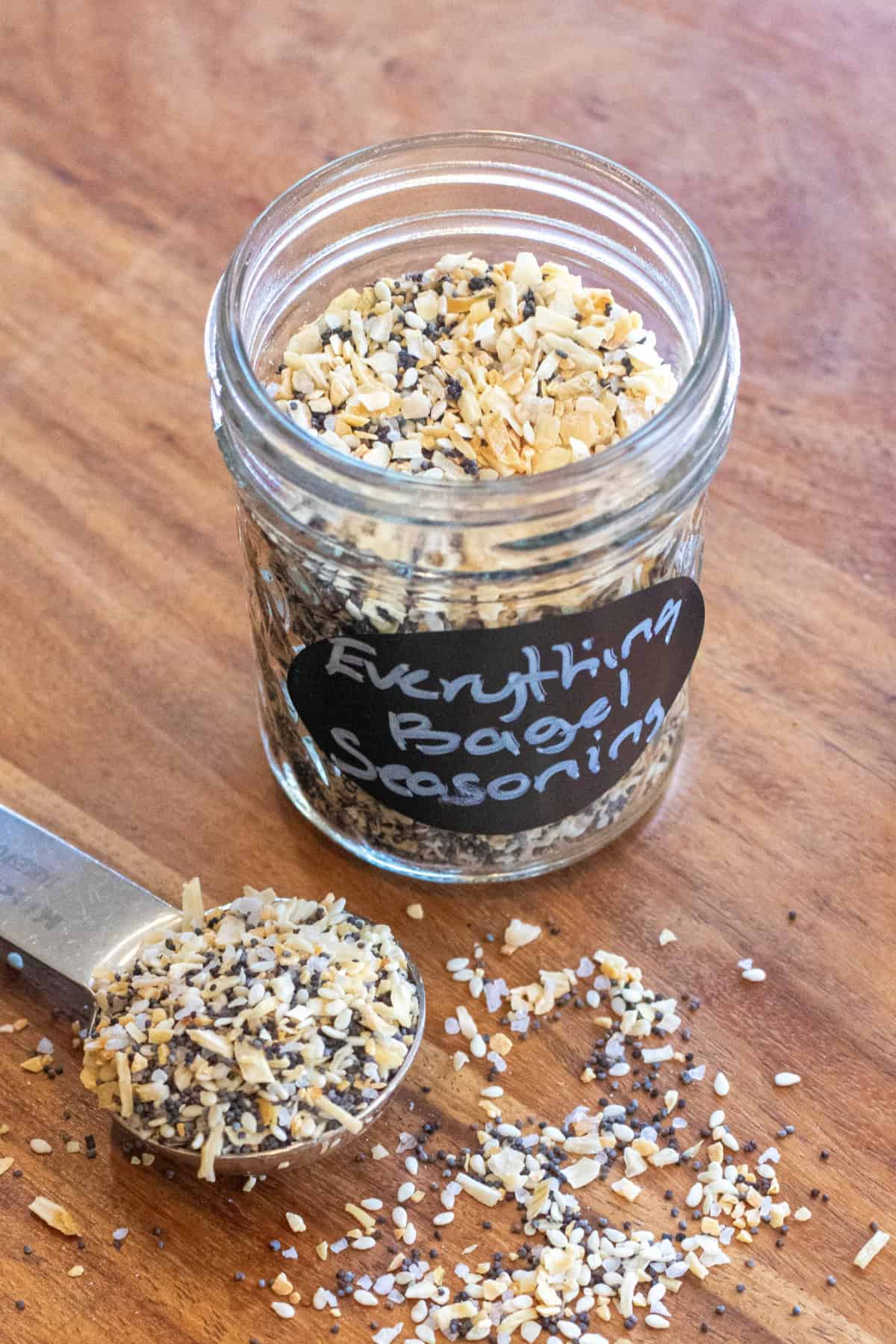 a labeled jar of everything bagel seasoning open with a tablespoon filled with seasoning next to it.