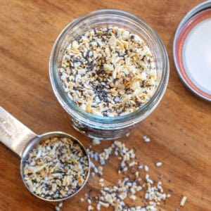 an overhead of a jar of everything bagel seasoning and a tablespoon with some in it.