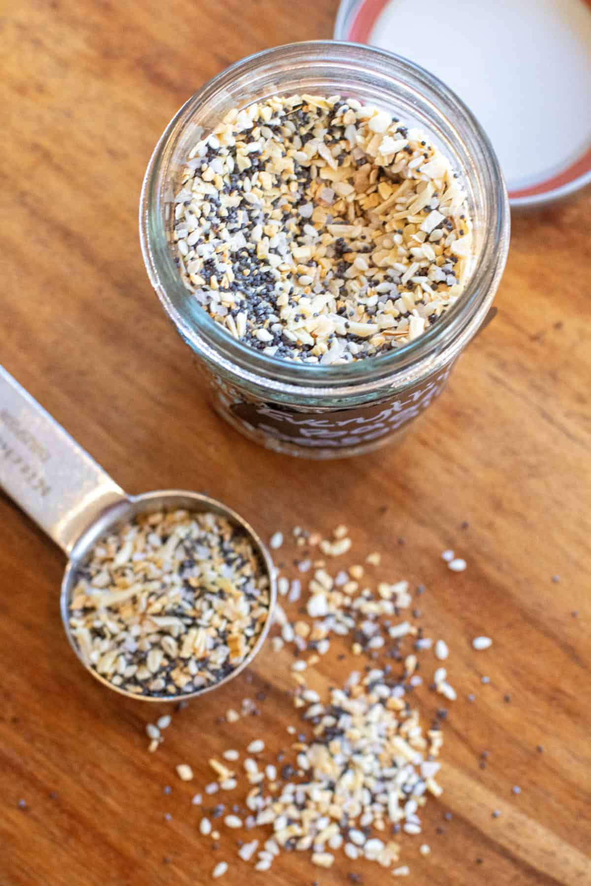 an overhead of a jar of everything bagel seasoning and a tablespoon with some in it.