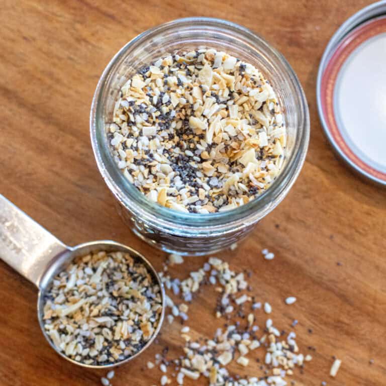 an overhead of a jar of everything bagel seasoning and a tablespoon with some in it.