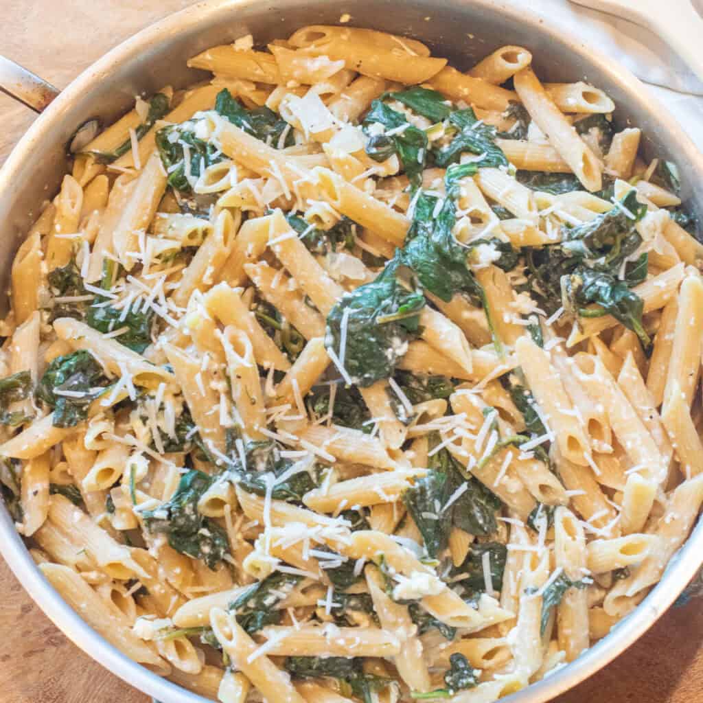 an overhead of a pan of spinach in penne pasta and shredded cheese.