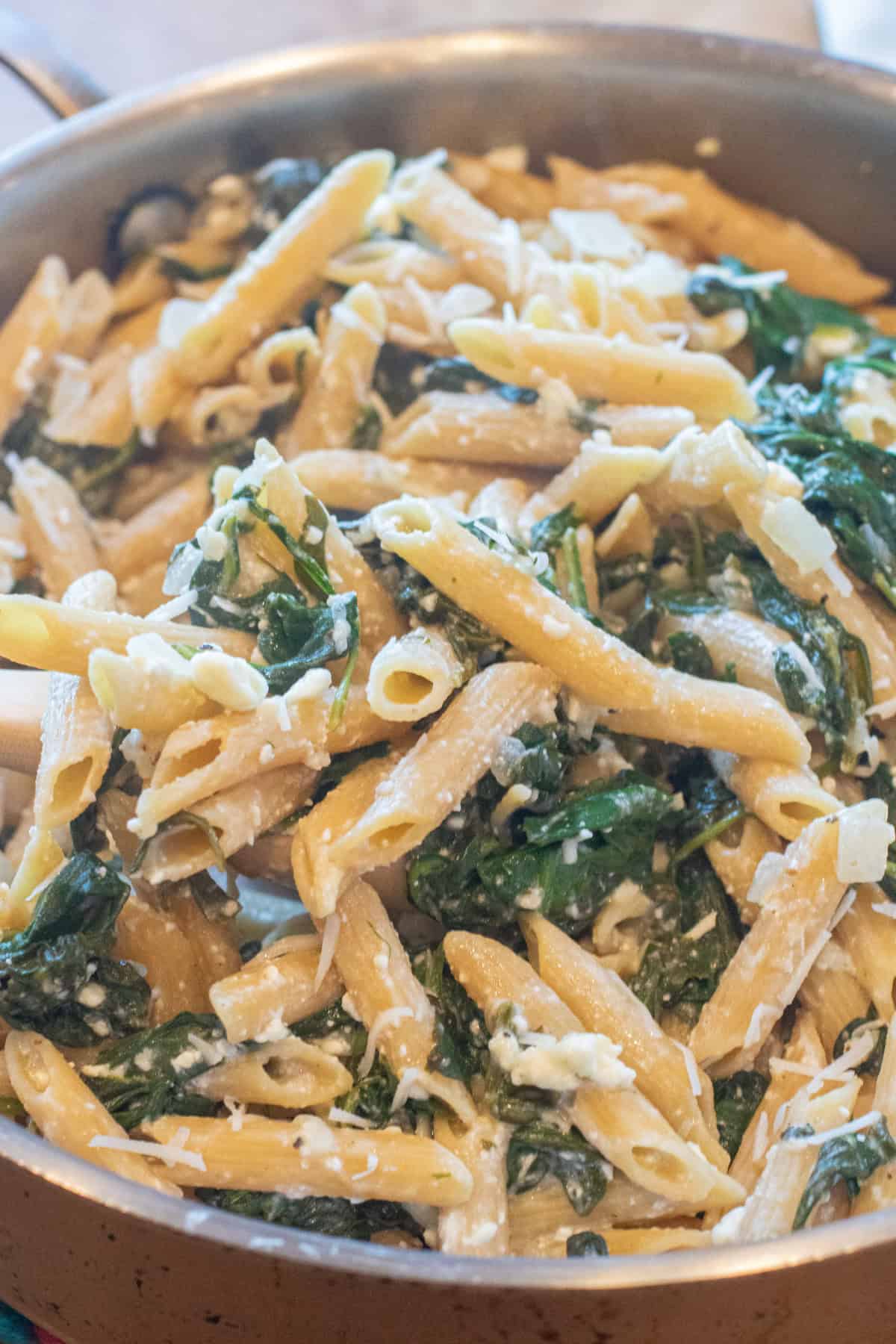 an overhead of a pan of spinach in penne pasta and shredded cheese.