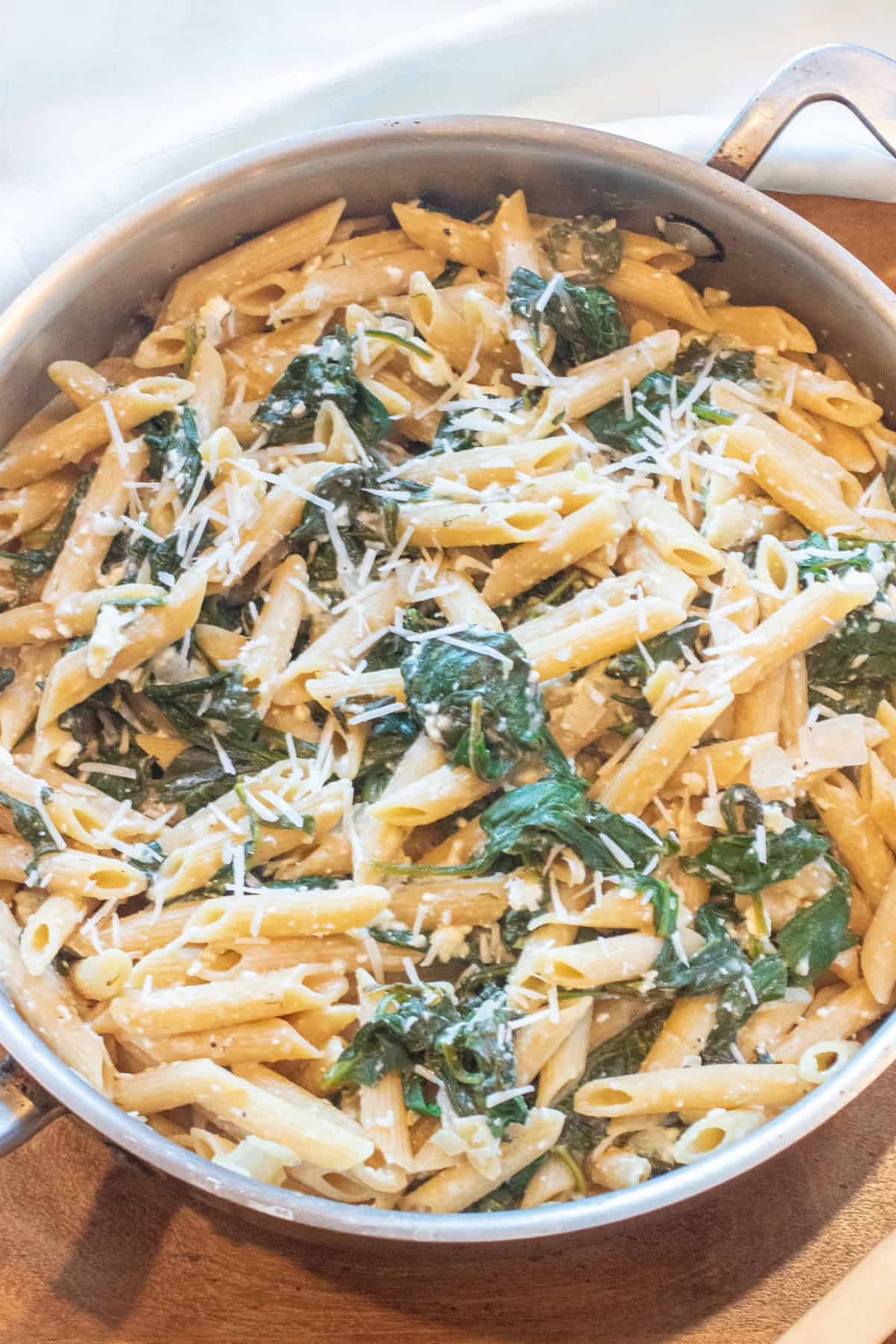 an overhead of a pan of spinach in penne pasta and shredded cheese.