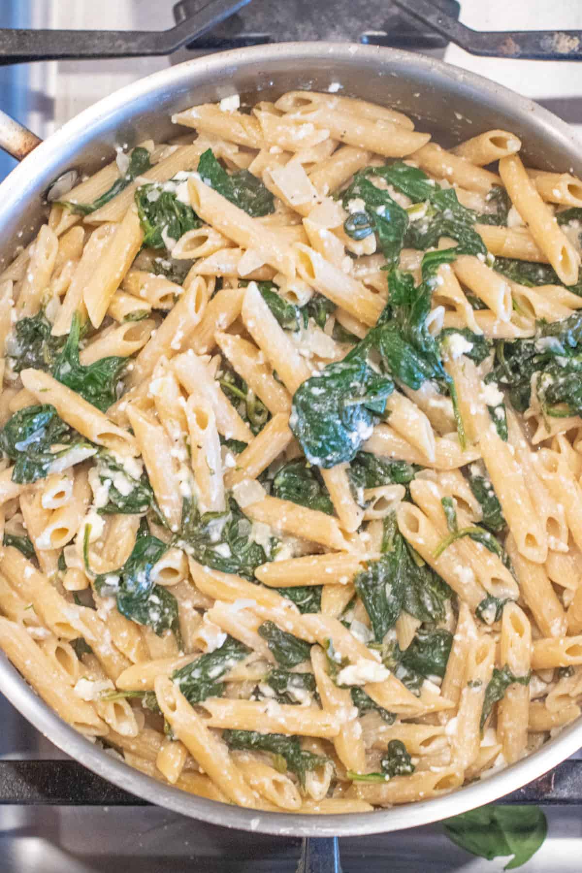 an overhead of a pan of spinach in penne pasta and shredded cheese.