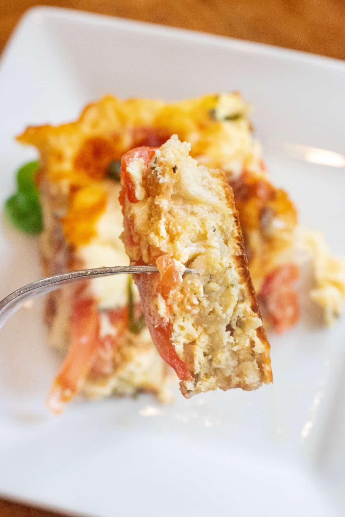 a piece of egg and tomato cheese and basil casserole on plate and a fork holding up a piece.