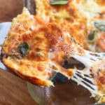 a piece of breakfast casserole with browned cheese and basil being pulled from a dish with a cheese pull.