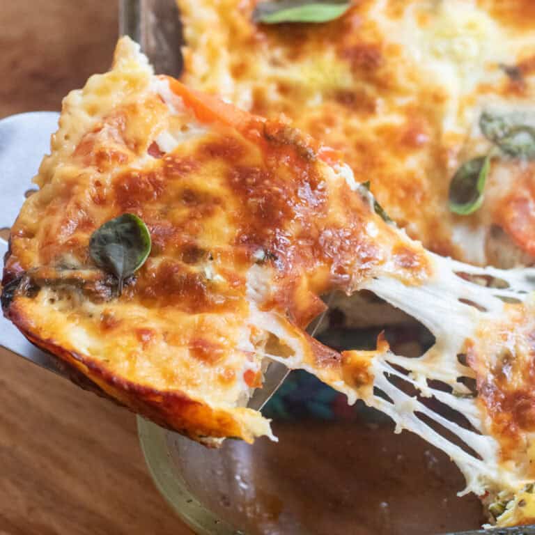 a piece of breakfast casserole with browned cheese and basil being pulled from a dish with a cheese pull.