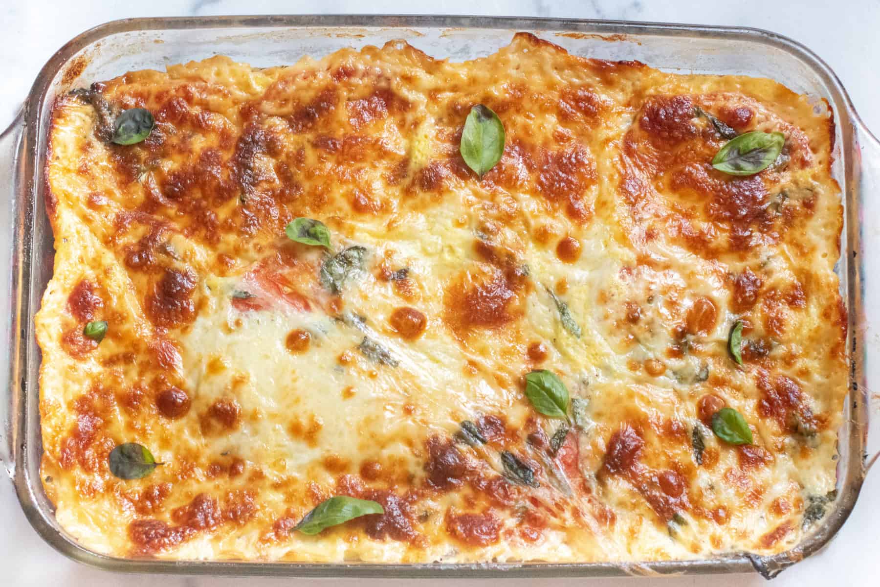 an overhead of a cheesy baked casserole with fresh basil.