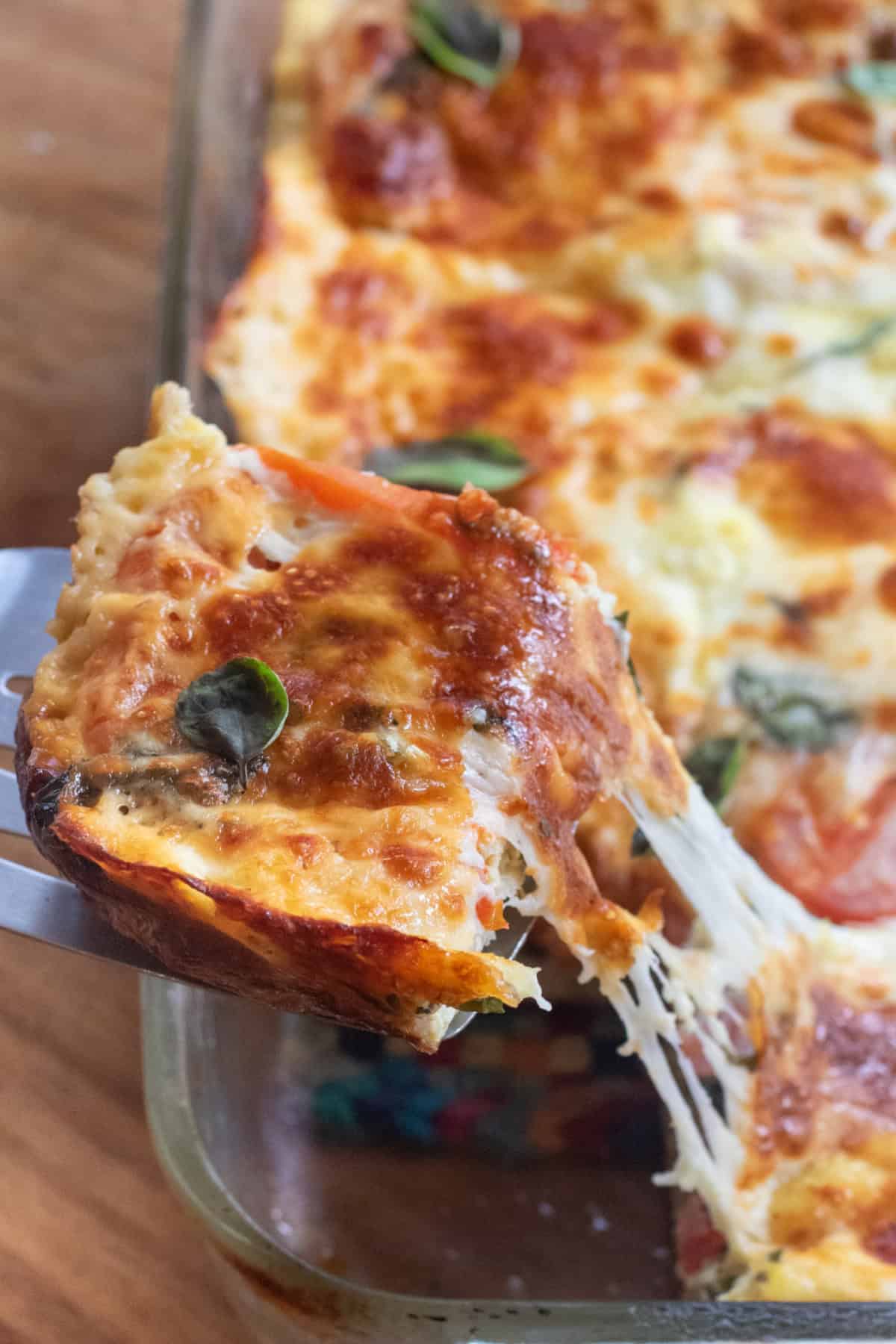 a sliced of cheesy egg casserole being pulled out of the baking dish with a cheese pull.
